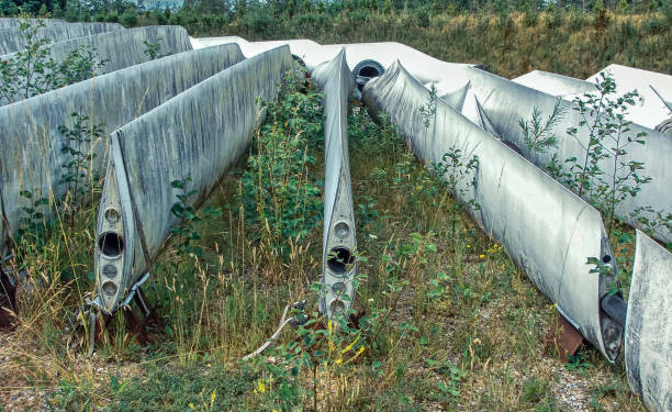 Old and abandoned wind turbine blades left deteriorating on a grassy field. The blades are made from fibreglass.