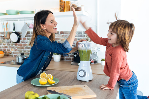 Shot of pretty young mother and her son giving high five after preparing a detox smoothie together in the kitchen at home.