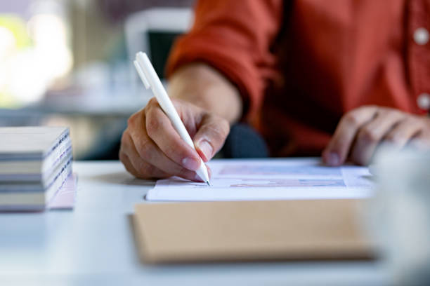 close up shot of hands of a irreconhecível businessman writing on a financial report - red pen paper document - fotografias e filmes do acervo