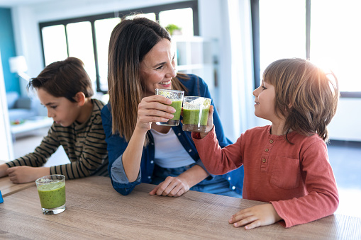 Shot of pretty young mother with her son toasting with detox smoothie in the kitchen at home.