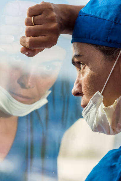 istock Overworked healthcare worker looking through a window, very concerned, very tired 1219594289
