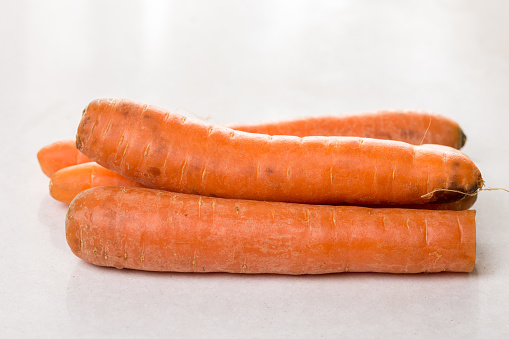 Fresh raw dirty carrot from the garden on the white marble background.