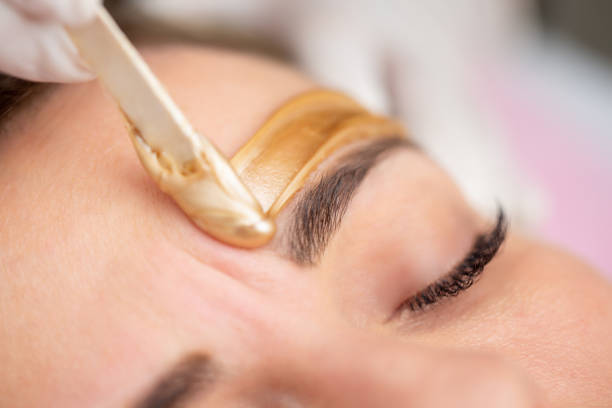 Applying Gold Colored Wax with Spatula on Woman's Face - stock photo Applying Gold Colored Wax with Spatula on Woman's Face waxing stock pictures, royalty-free photos & images