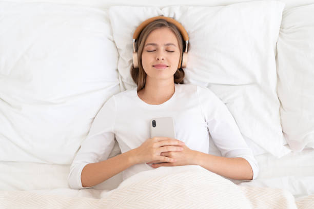 jeune femelle vêtue de blanc passant tard le matin dans le bâti, écoutant la musique ou le livre audio de son smartphone, rêvant ou relaxant - female likeness audio photos et images de collection