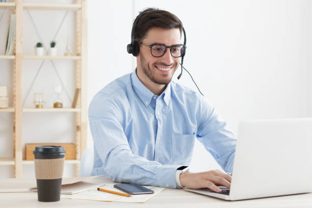 istock Guy in blue shirt working in office typing and checking data on his laptop while answering phone calls from client as worker of customer service 1219598112