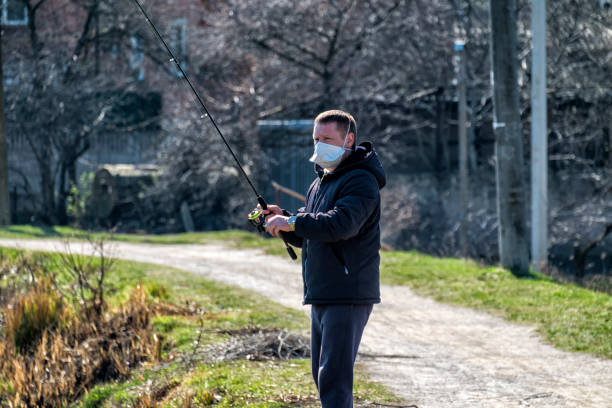 Fisherman with a spinning rod in his hands during an epidemic COVID-19 does not forget about quarantine rules Fisherman with a spinning rod in his hands during an epidemic COVID-19 does not forget about quarantine rules vinnytsia stock pictures, royalty-free photos & images