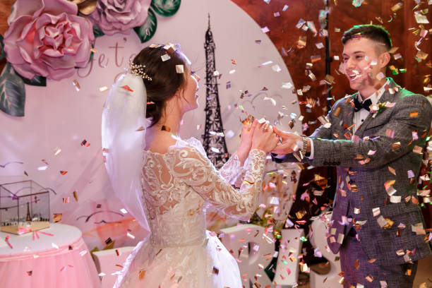 Happy bride and groom dancing under confetti at wedding reception. Newlyweds dancing their first dance with special effects. Decoration with inscription ''Je T'Aime'' on background