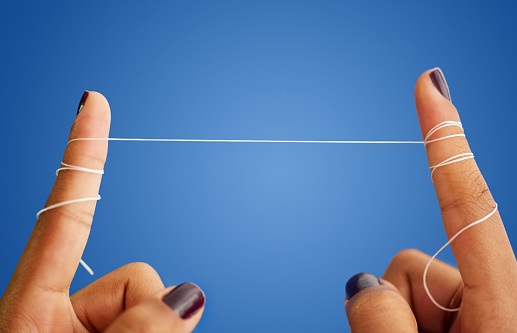 Close-up shot of a woman fingers holding dental floss against blue background