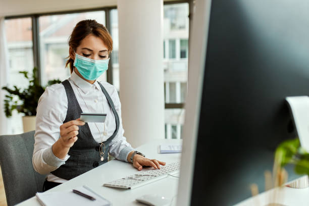 istock Businesswoman with face mask using credit card while e-banking in the office. 1219615819