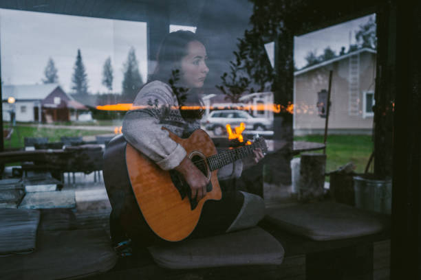 Low Angle Portrait Of Beautiful Woman Playing Guitar While Sitting By Window