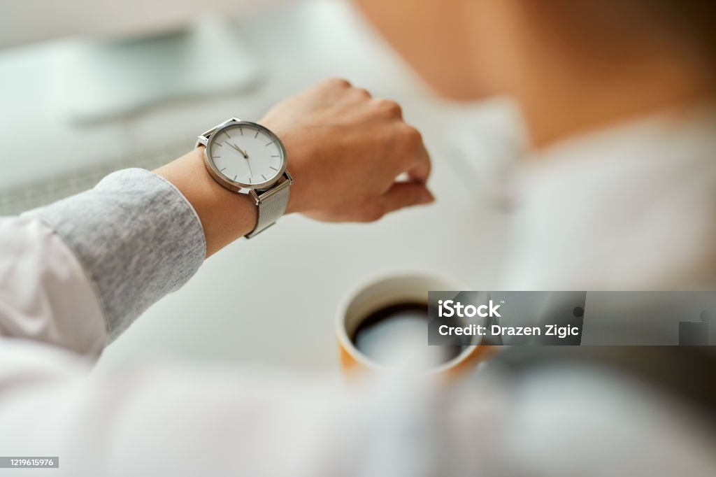 Close-up of businesswoman checking time on her wristwatch. Close-up of businesswoman looking at time on her wristwatch while having coffee break in the office. Clock Stock Photo