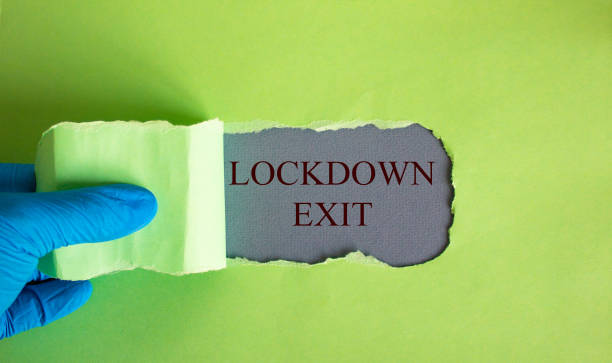 istock The text lockdown exit appearing behind torn yellow paper. Hand in blue glove. 1219623906
