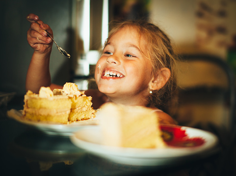 Happy little girl eating cake. Little funny girl with a smile eating cake.