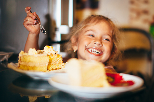 Happy little girl eating cake. Little funny girl with a smile eating cake.