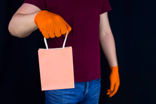 istock Delivery man wearing protective gloves holds paper gift bag 1219631257