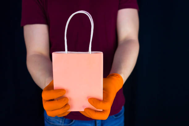 istock Delivery man wearing protective gloves holds paper gift bag 1219631271