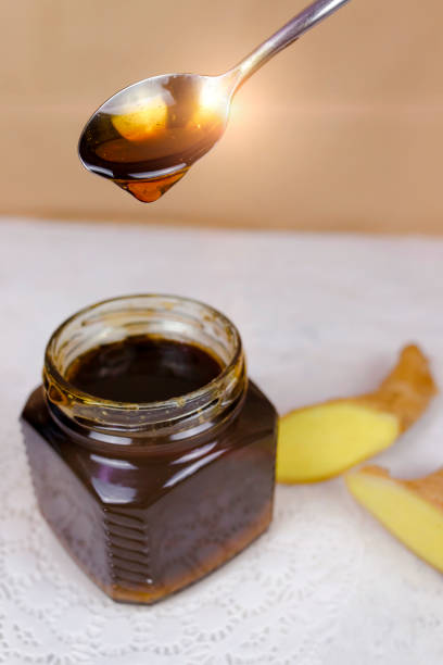 istock Buckwheat honey pours from spoon into jar and sliced ginger lying near. 1219631821