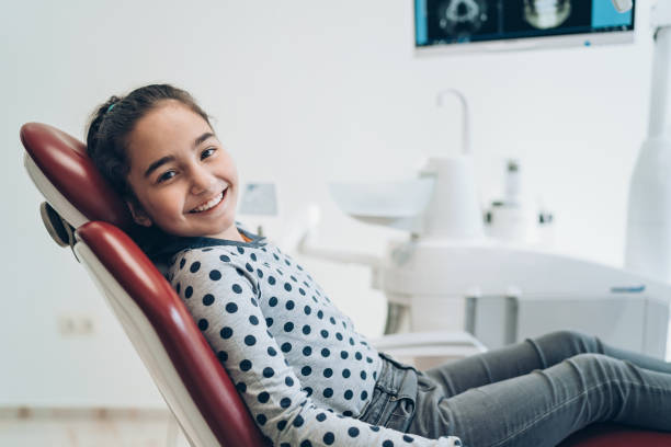 lächelndes mädchen sitzt auf dem zahnarztstuhl - teenager dentist patient cheerful stock-fotos und bilder