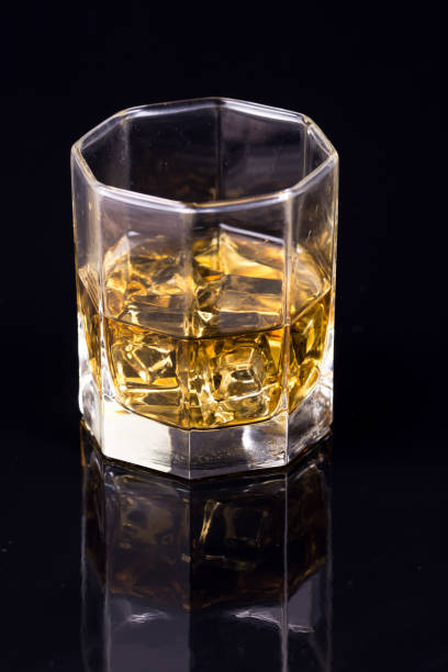 反射のある黒い背景にウイスキーとアイスキューブを持つ八角形のガラス - whisky glass ice cube alcohol ストックフォトと画像