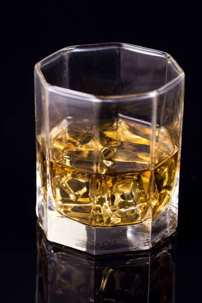 反射のある黒い背景にウイスキーとアイスキューブを持つ八角形のガラス - whisky glass ice cube alcohol ストックフォトと画像