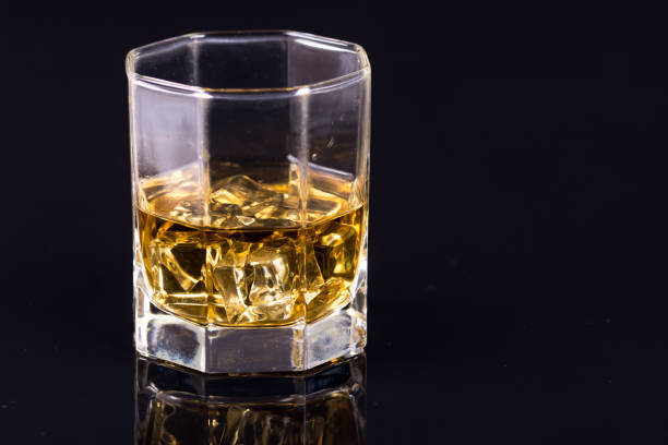 反射のある黒い背景にウイスキーとアイスキューブを持つ八角形のガラス - whisky glass ice cube alcohol ストックフォトと画像