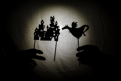 Chinese shadow theater for children projected on a bed sheet, themed of Saint George, April 23. The shadows are of cardboard with a little basset, you can also see the hand that manipulates them. tales, the fairy, storyteller.