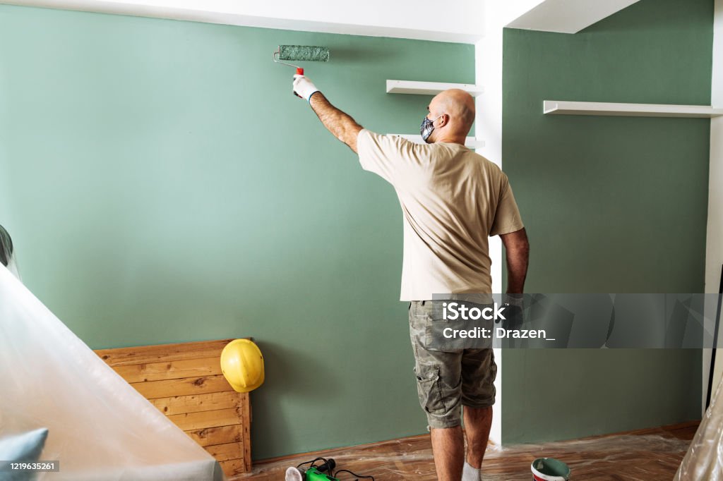 Mature man enjoys home improvement and painting the walls during Coronavirus lockdown Renovation during quarantine - DIY at home, family painting walls in living room and changing the interior Painting - Activity Stock Photo