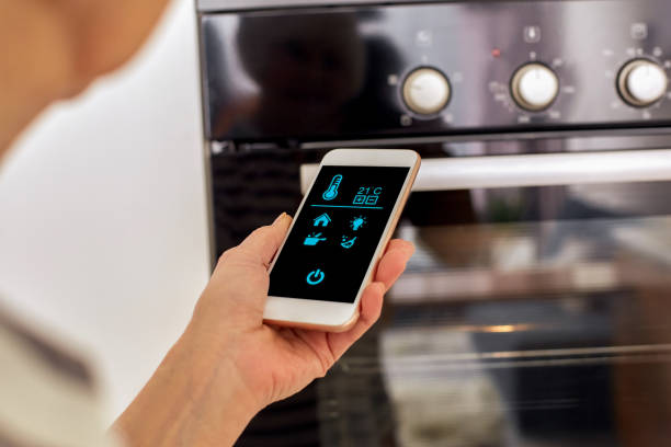Female woman hand holding mobile phone use voice assistant smart home remote system. Online shopping customer delivery indoors. White mockup camera device monitoring house. Lady cook help turn on oven mujer mujer mano sosteniendo el teléfono móvil utilizar asistente de voz inteligente hogar remoto sistema remoto. entrega de clientes de compras en línea en interiores. casa de monitoreo de dispositivos de cámara de maqueta blanca. señora cook ayuda e