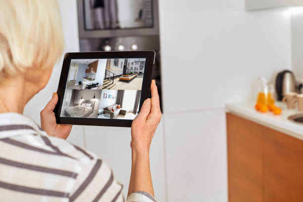 istock Retirement. Senior woman standing controlling smart home on digital tablet back view checking cameras close-up 1219641813