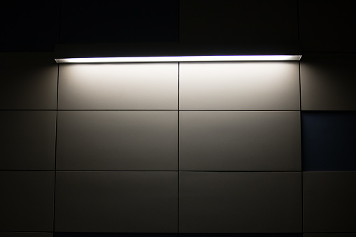 Fluorescent light inside the underground metro station. Rectangular tiles on the wall.