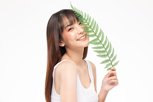 Young Beautiful Asian woman smile with clean and fresh skin with green leaf cover on face,isolated on white background,Beauty Cosmetics and spa Treatment Concept