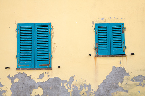 Blue windows on yellow wall in historic Lucignano, Tuscany, Italy