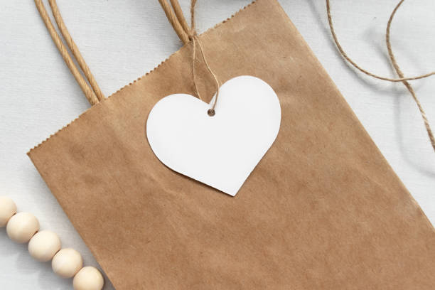 istock Blank white gift luggage tag on a brown paper bag - Flat lay gift tag mockup 1219661696