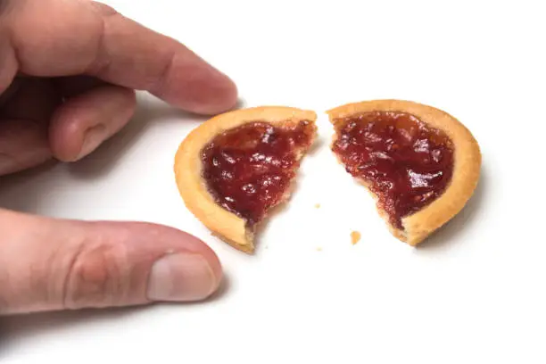 Closeup of crunched mini tartlets with strawberry jam in hand on white background