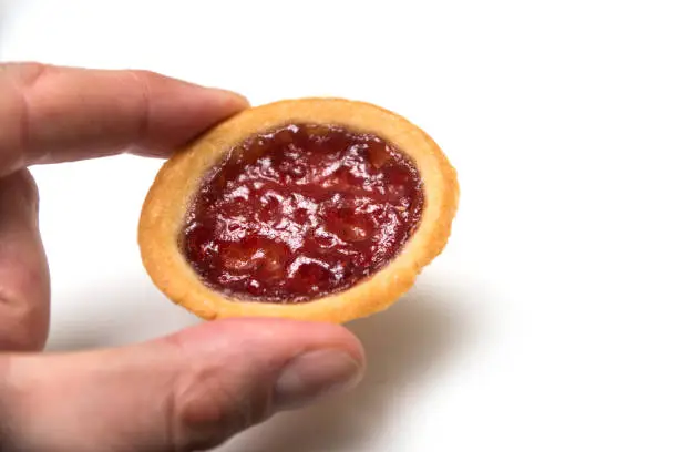 Closeup of mini tartlet with strawberry jam in hand on white background