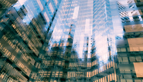 Abstract background of modern skyscrapers with glass walls reflecting each other in a mirroring effect. Soft pastel colors with brown and blue hues. Shiny glass and surreal atmosphere contribute to a dramatic abstract background. Daylight with no people. Digitally generated image.