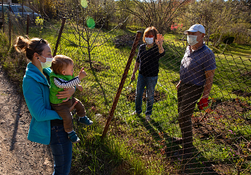 Family members with protective masks communicating across a fence outside the city