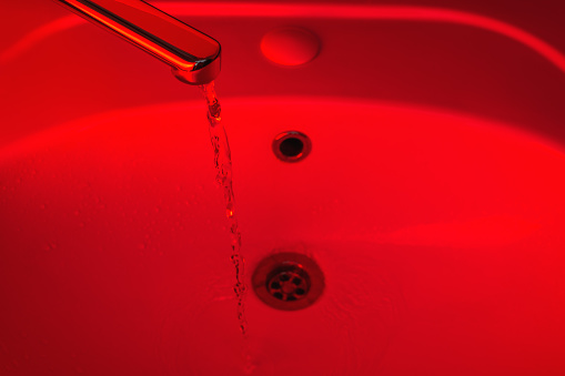 Water runs from the tap in the bathroom with a red light. Bathroom with red light. Hygiene concept for protection against coronavirus infection.
