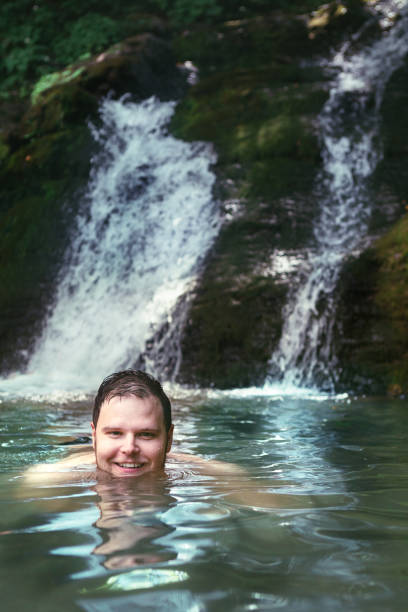 istock young smiling man swimming in lake with waterfall on background 1219679376