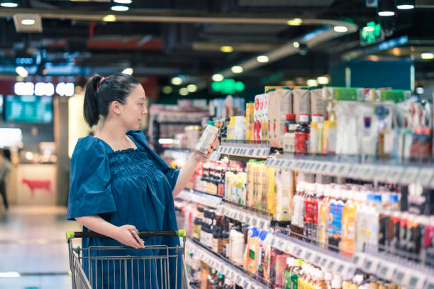 donna incinta asiatica che fa la spesa al supermercato e sceglie la salsa in bottiglia - human pregnancy clothing shopping retail foto e immagini stock