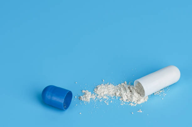 istock Close up opened medicine capsule pill with powder on blue background. 1219685700