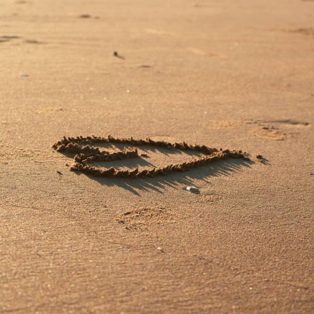 A heart shape etched in warm sand, surrounded by gentle footprints on a serene beach at dusk.