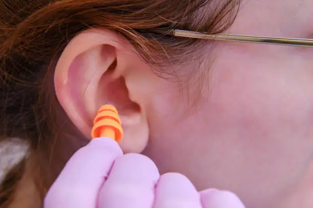 A woman inserts earplugs into her ear in protective medical gloves, close-up