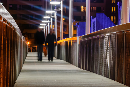 Two men walk along a pedestrian bridge at night