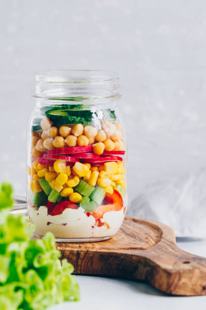 istock Layering salad in a glass jar. Fresh radish, cucumber, celery, red bell pepper, corn, chickpeas and sauce. 1219698021