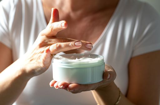 Female hands holding a jar of facial cream and taking a little bit with her finger for application