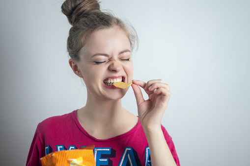 Smiling young Caucasian woman girl eating biting potato chips crisps ,
