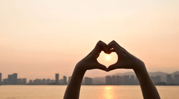 Woman hand make a heart shape in sunset.