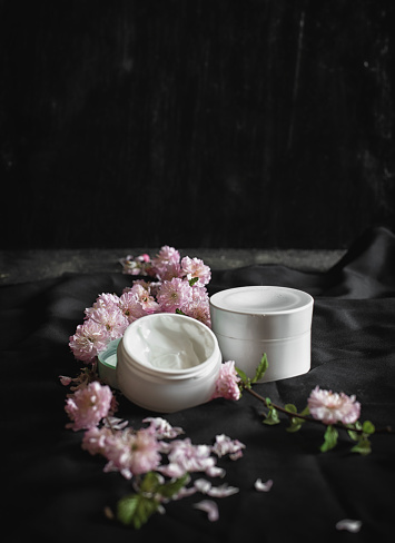 picture of two white cream pots on the black background with pink flowers