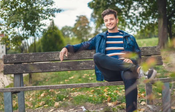 istock Positive young man with smile on his face sitting on bench 1219706892